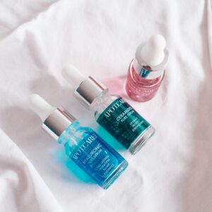 Selection of colorful skincare serums in glass bottles on a white background.