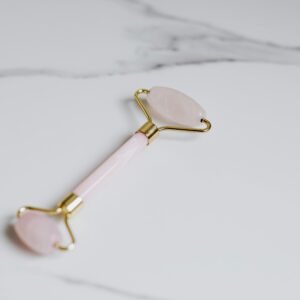 Elegant rose quartz facial roller placed on a marble surface for beauty and skincare.