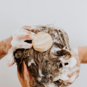 Close-up of a person washing their hair with soap bar and foam, focusing on hands and hair.