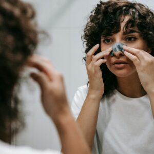 Adult woman applying a nose strip as part of her skincare routine in front of a bathroom mirror.