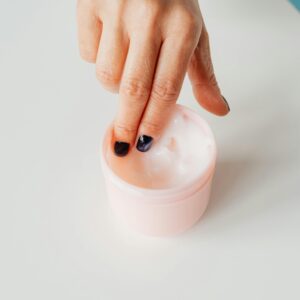 Close-up of a hand with painted nails dipping into a jar of face cream, representing self-care.